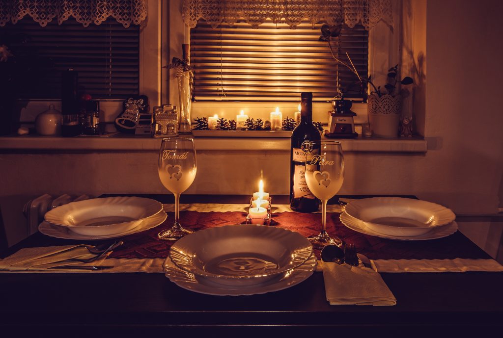 Set up the dining table for dinner with loads of candles, tableware and glasses of wine.